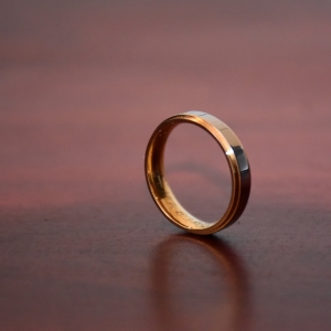 A single gold wedding ring stands on its edge on a wooden table