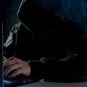 person in dark hoodie sits at the computer screen you can only see his hands 