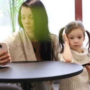 mother looking at her mobile phone with young daughter standing beside her also holding a mobile phone