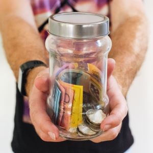 A man's hands holding a jar full of notes and coins